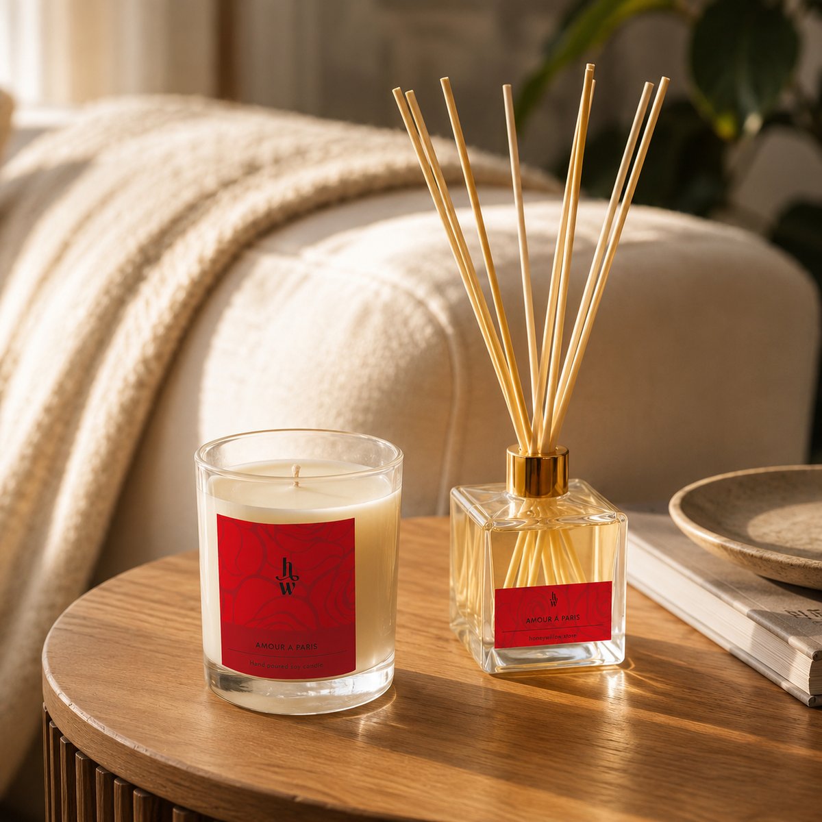 The Amour a Paris candle and reed diffuser on a wooden side table beside a cream knit throw