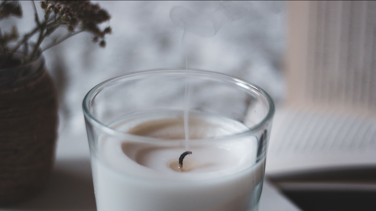 A glass soy candle burning with a full, even melt pool by a bright window