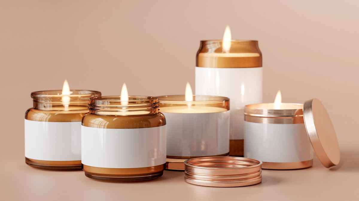 A set of amber glass soy candles with copper lids on a soft pink background