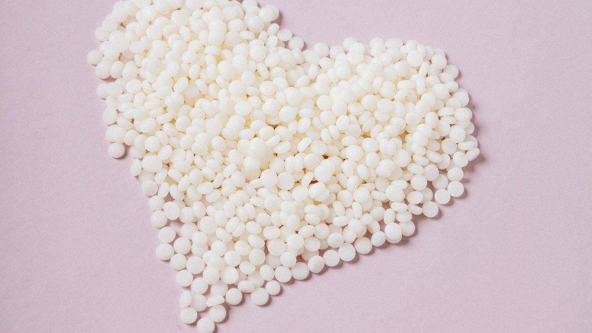 White soy wax flakes arranged into a heart shape on a soft pink background