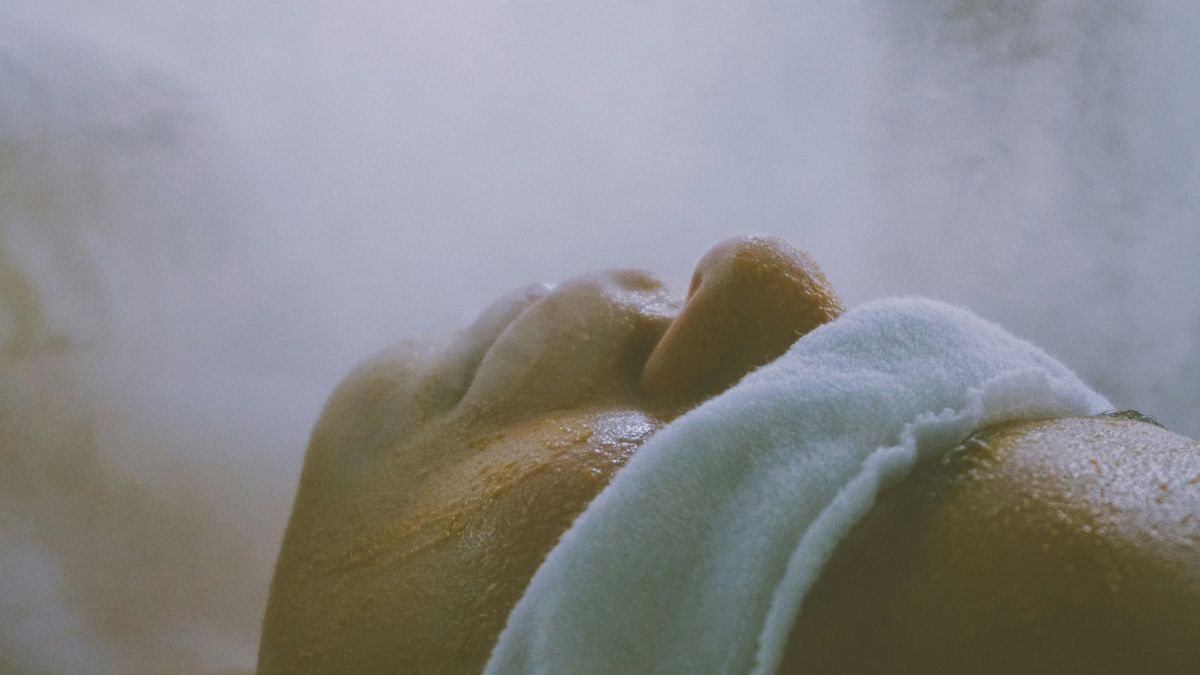 A person relaxing with closed eyes and a soft towel amid gentle steam in a calming setting