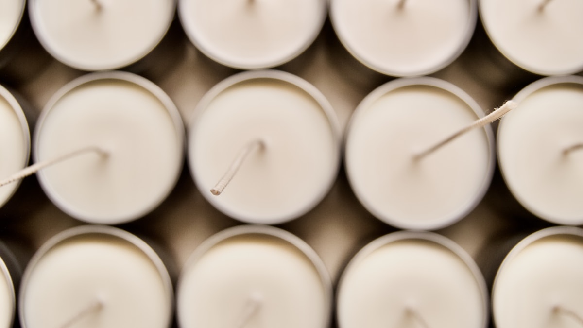 Rows of unlit white candles seen from above with their natural cotton wicks visible