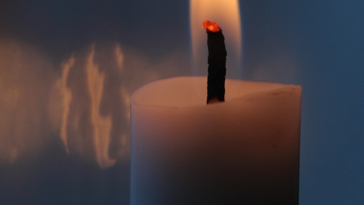 White soy candle burning with a tall dark wick tip mushrooming above the flame