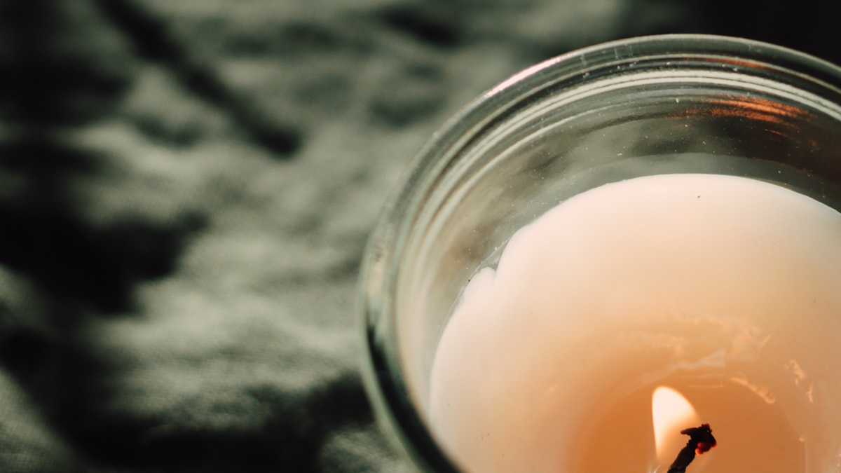 Soy candle in a clear glass jar resting on dark linen fabric, seen from above